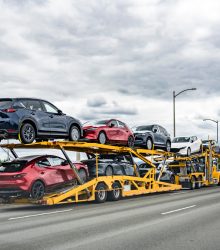 Professional powerful yellow big rig industrial car hauler semi truck with two level modular hydraulic semi trailer transporting cars moving on the wide multiline highway road with stormy sky
